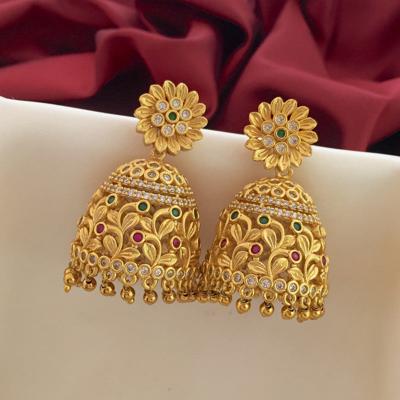 A pair of ornate gold jhumka earrings with floral stud tops, intricate designs, and small dangling beads, adorned with green, red, and white stones.