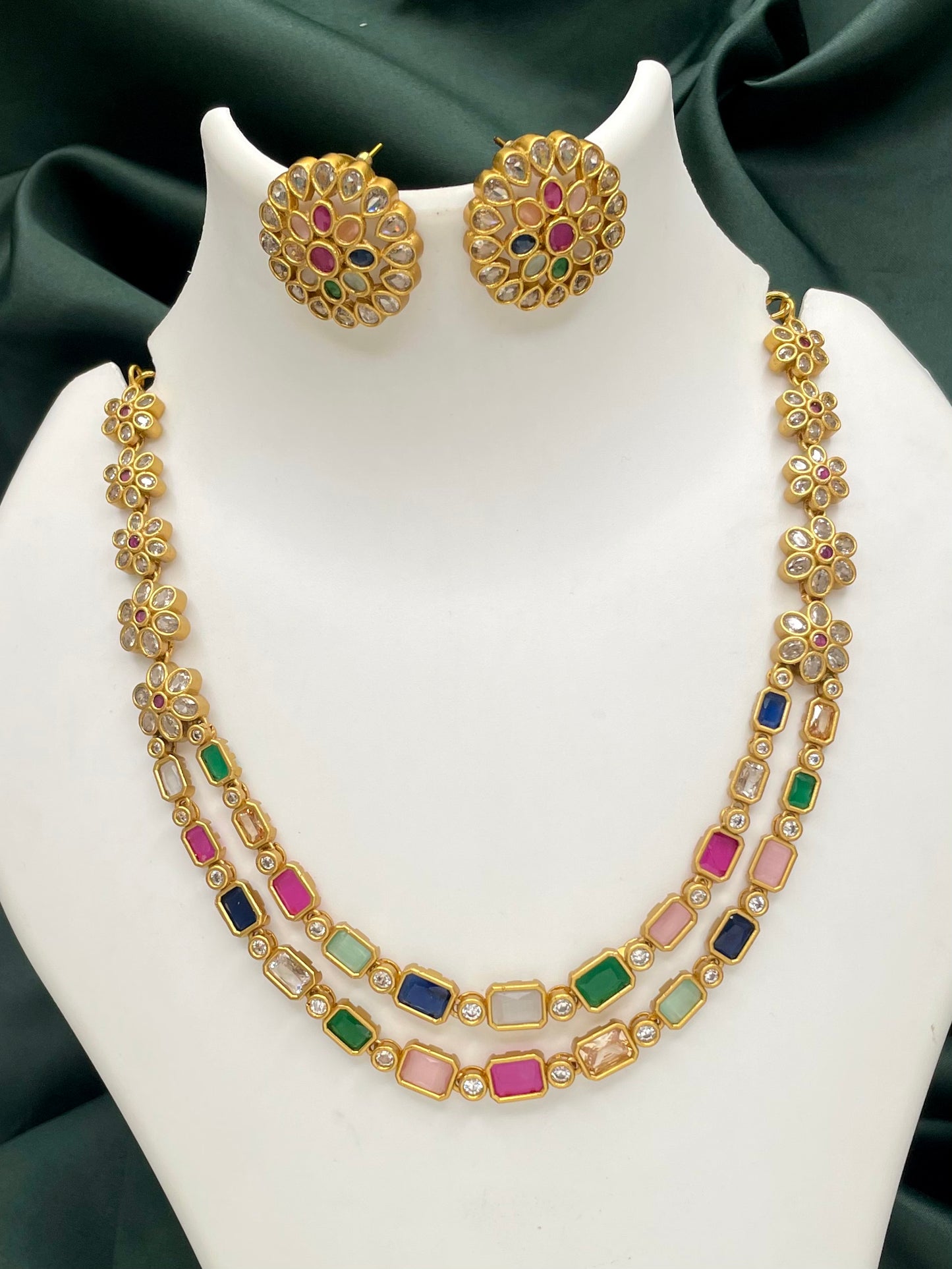 A gold necklace with multicolored gemstones and matching round earrings.