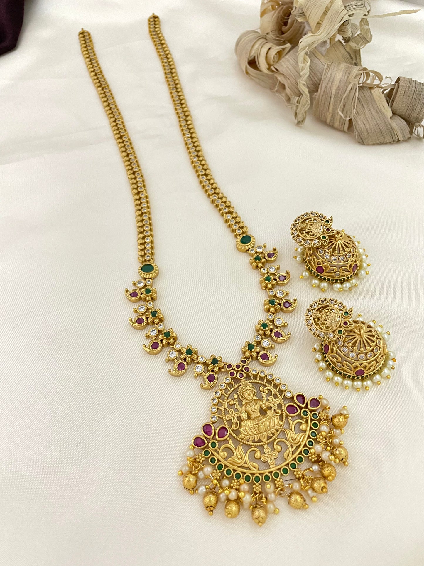 A gold necklace with intricate designs, featuring a large pendant with a deity figure, accompanied by matching earrings.