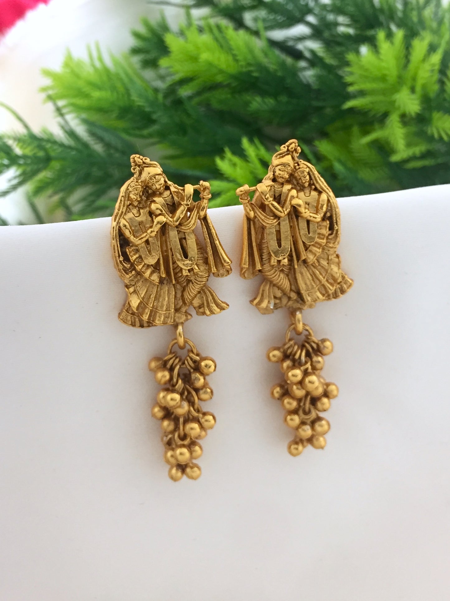 Gold-toned earrings featuring intricate designs of two figures and dangling bead clusters.