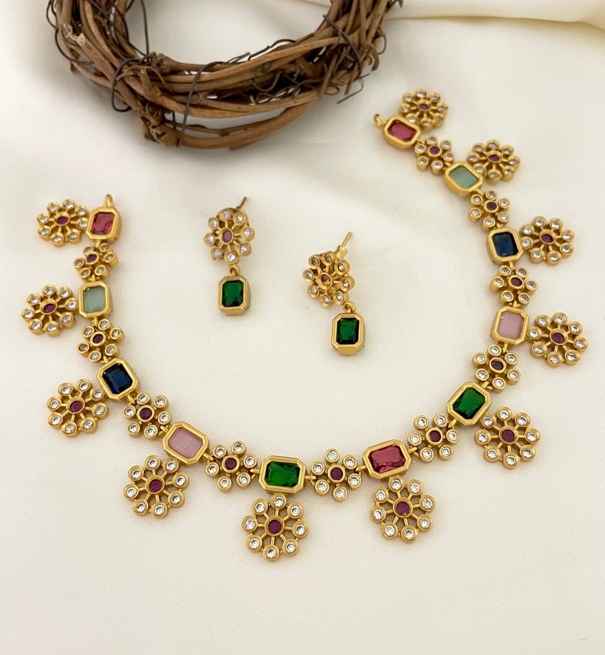 Gold necklace and earrings set with multicolored gemstones and intricate floral designs.