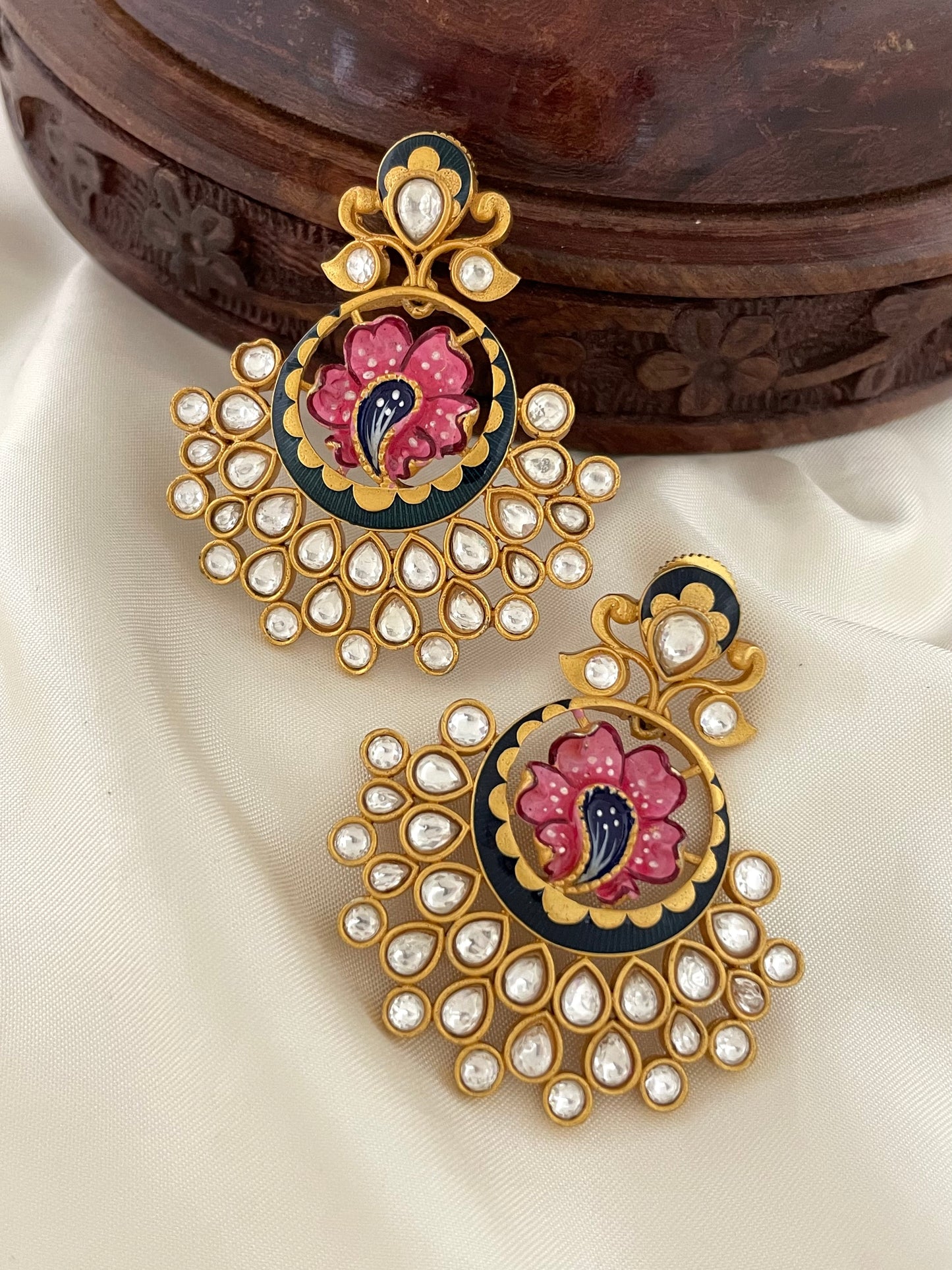 A pair of ornate gold earrings with intricate floral designs and embedded white gemstones.