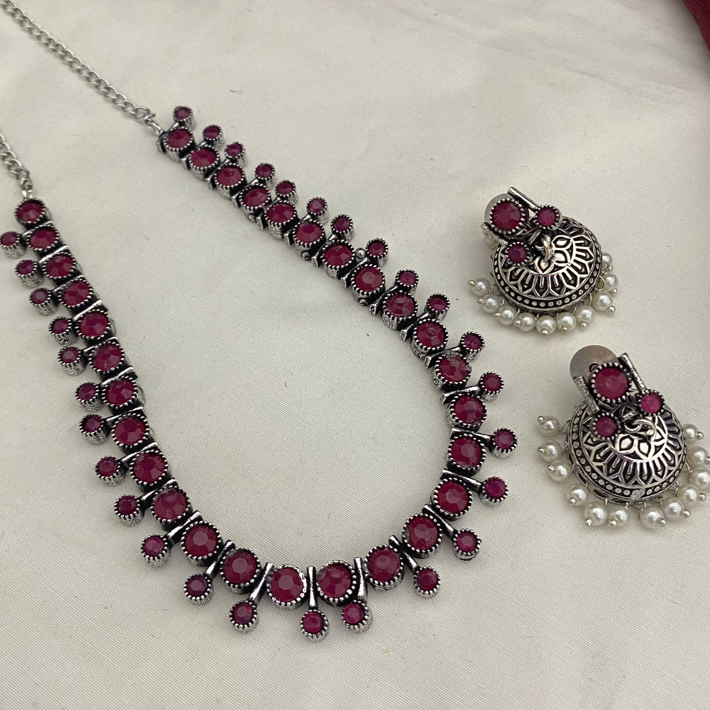 A silver necklace and matching earrings with red stones and pearl accents.