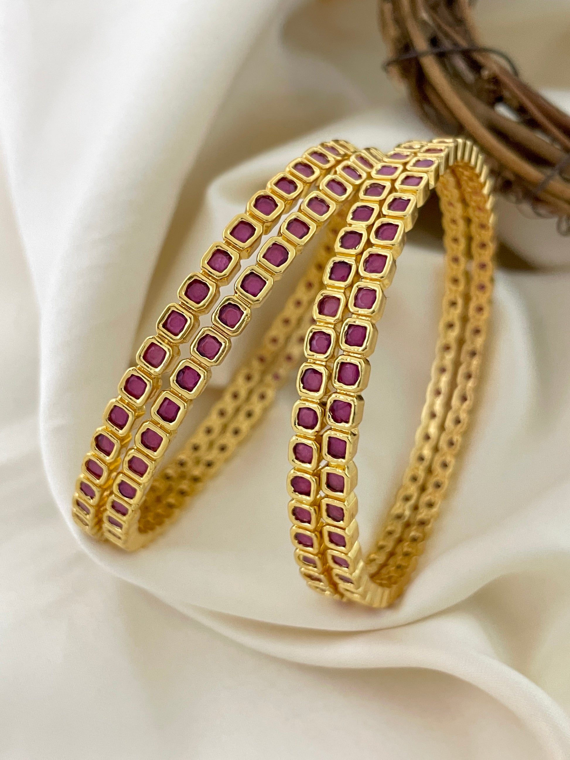 Two gold bangles adorned with small square red gemstones.