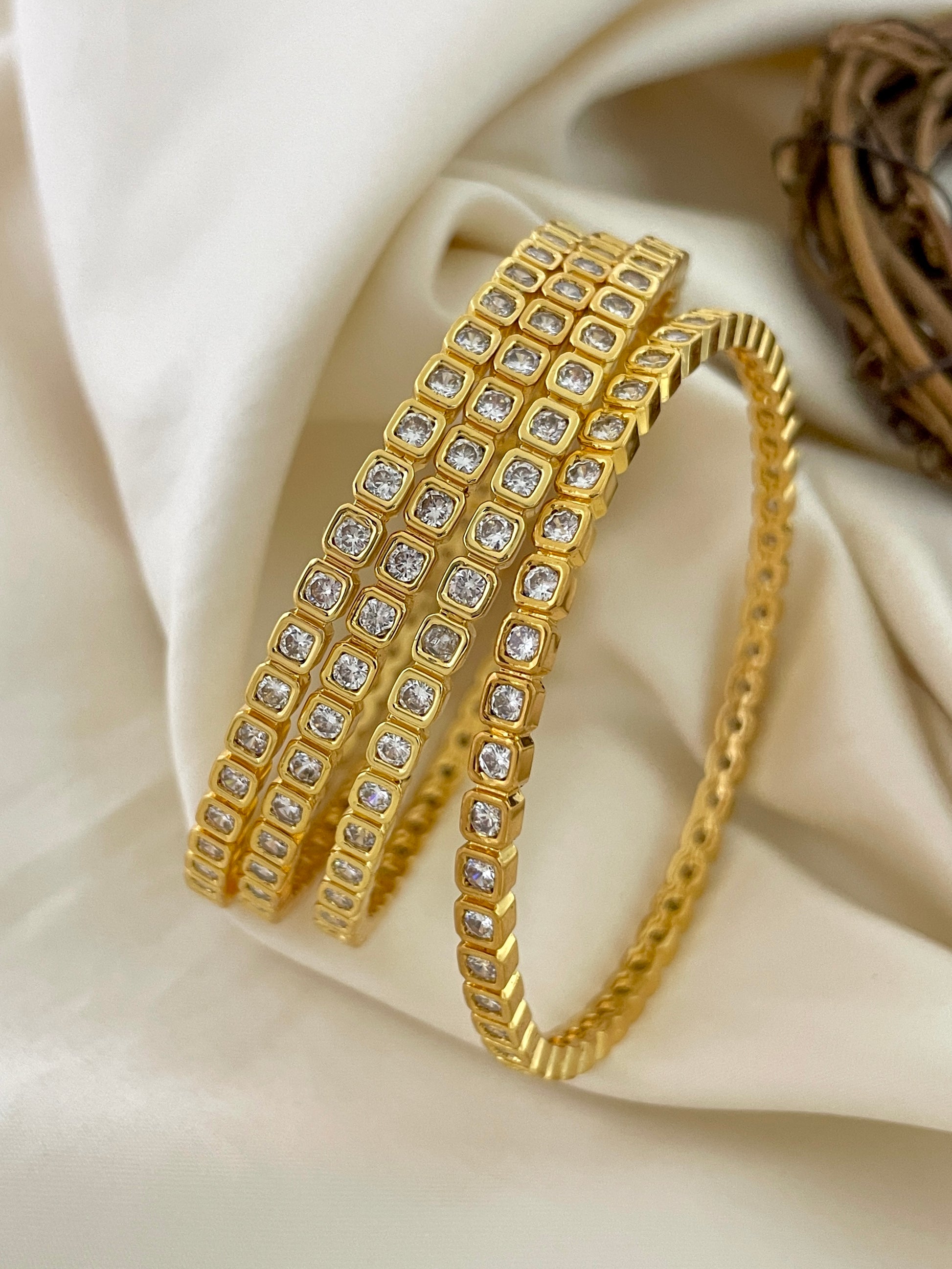Three gold bangles adorned with square-shaped diamond-like stones.