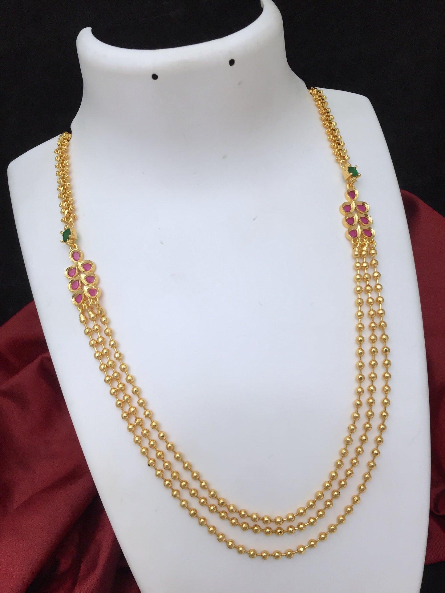 Gold necklace with three layers of beads and floral designs featuring pink and green gemstones.
