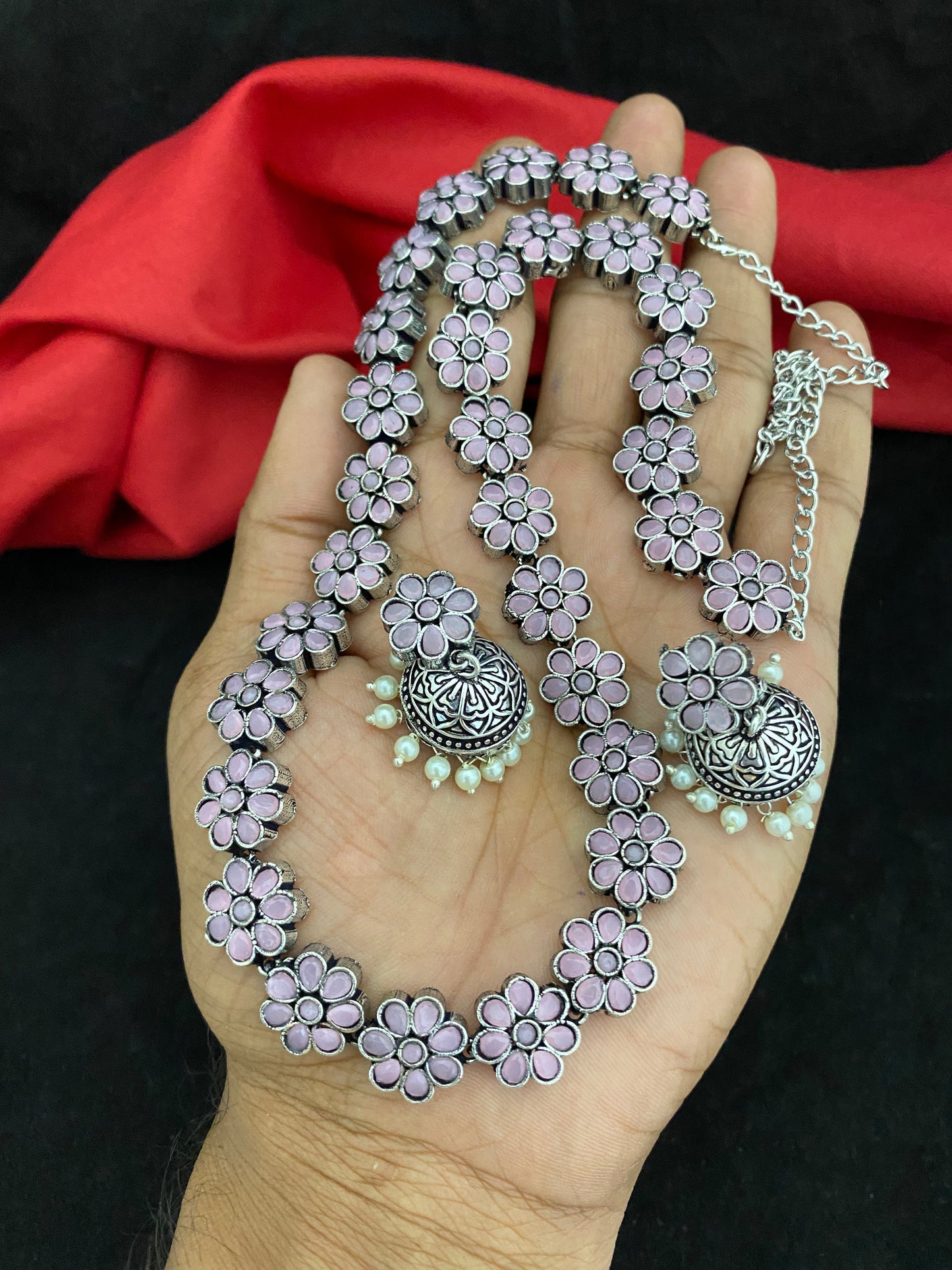 A hand holding a floral necklace and matching earrings with purple petals and silver detailing.