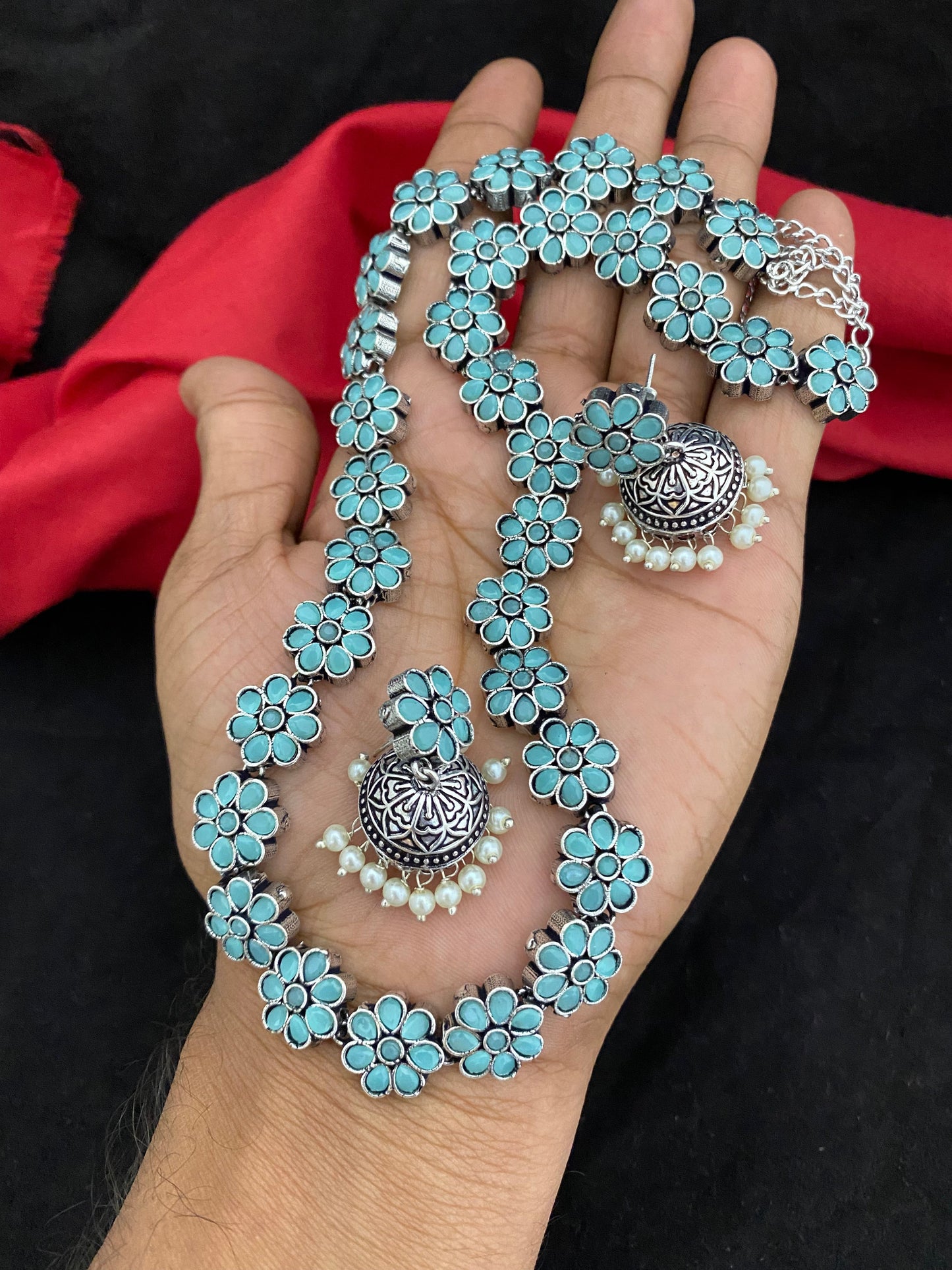 A hand holding a turquoise floral necklace with matching earrings.