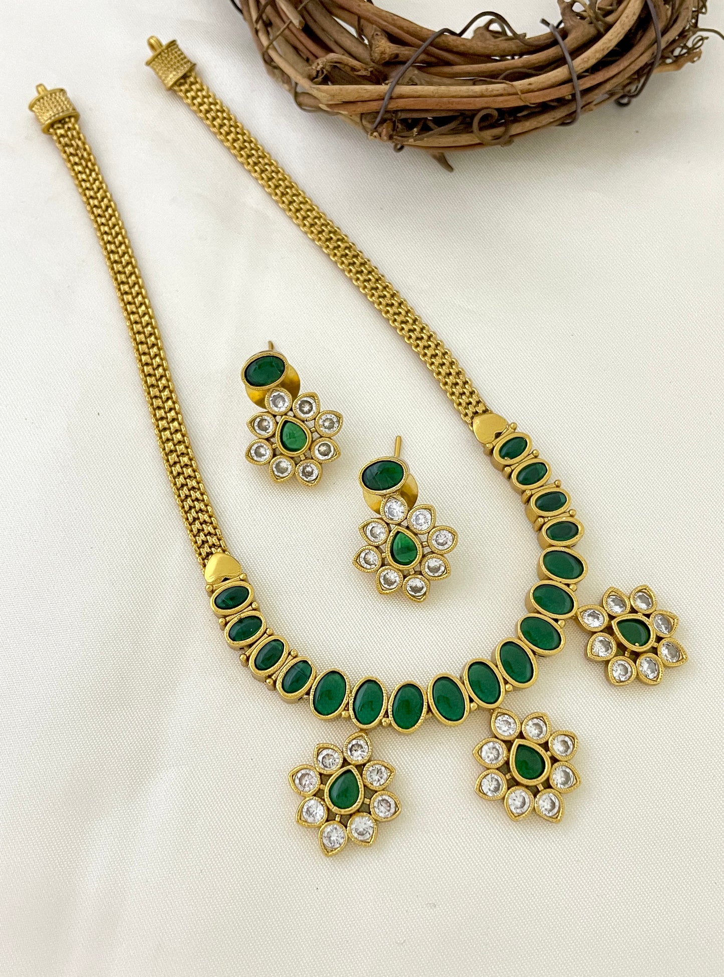 A gold necklace with green oval stones and matching earrings featuring green and white stones.