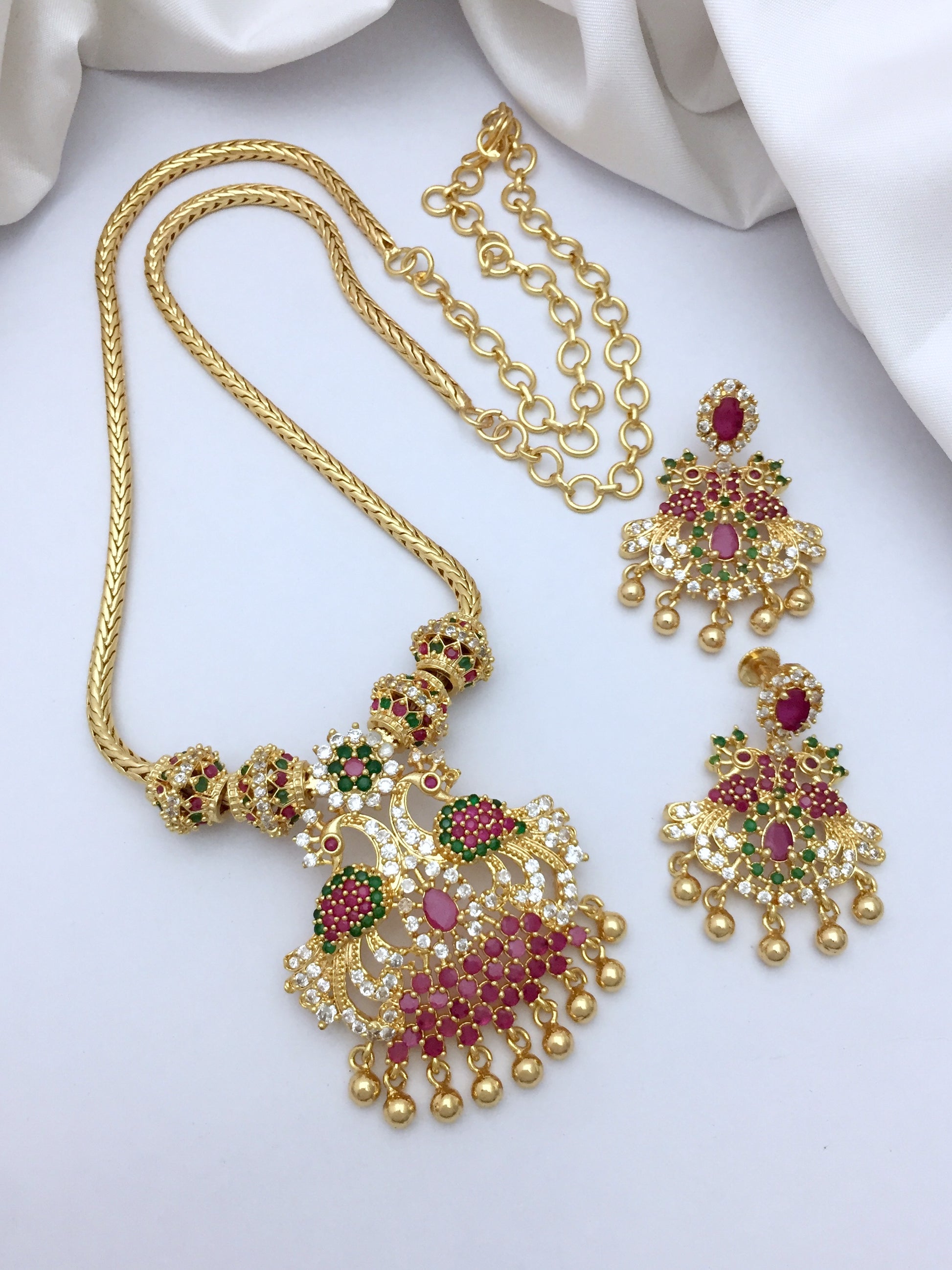 A gold necklace with an intricate pendant featuring red, green, and white stones, accompanied by a matching pair of earrings.