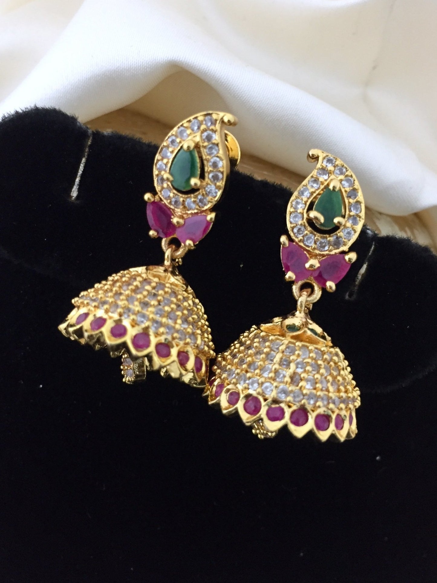 Gold jhumka earrings with multicolored stones, featuring a teardrop design with green and red stones and intricate detailing.