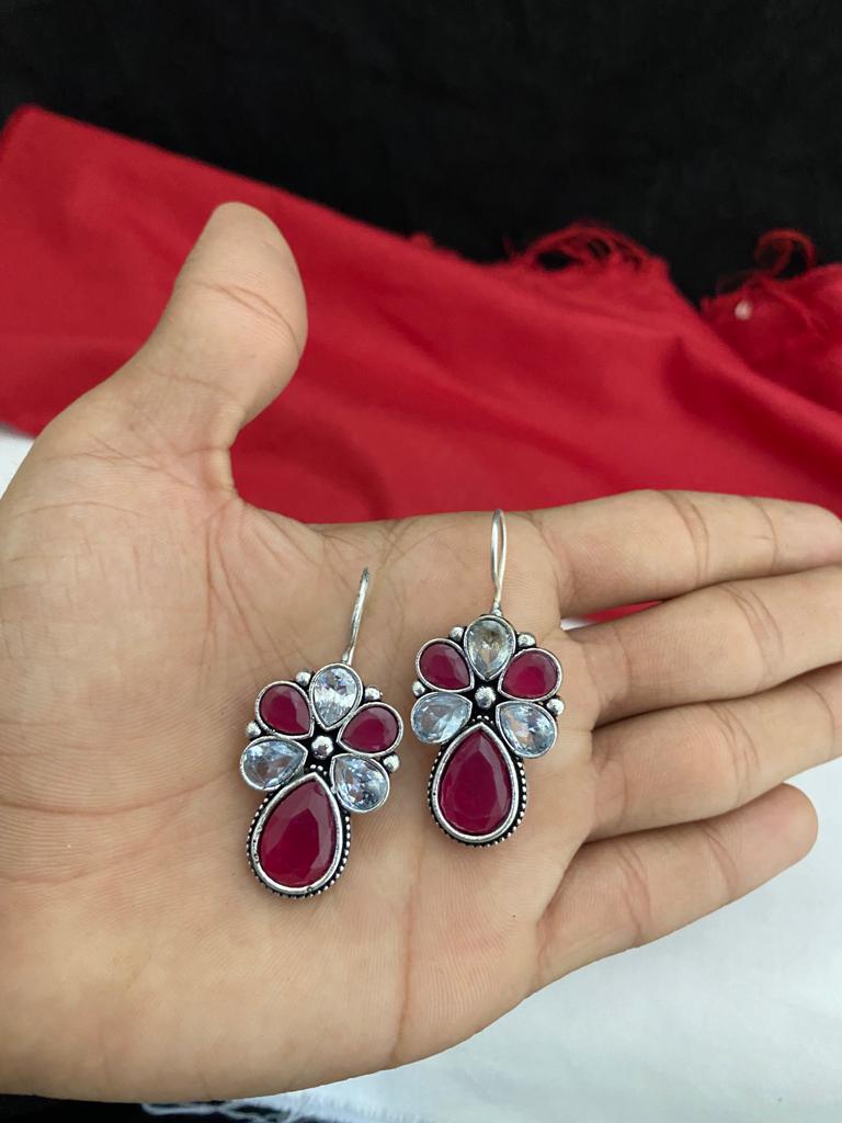 A pair of silver earrings with red and clear gemstones held in a hand.