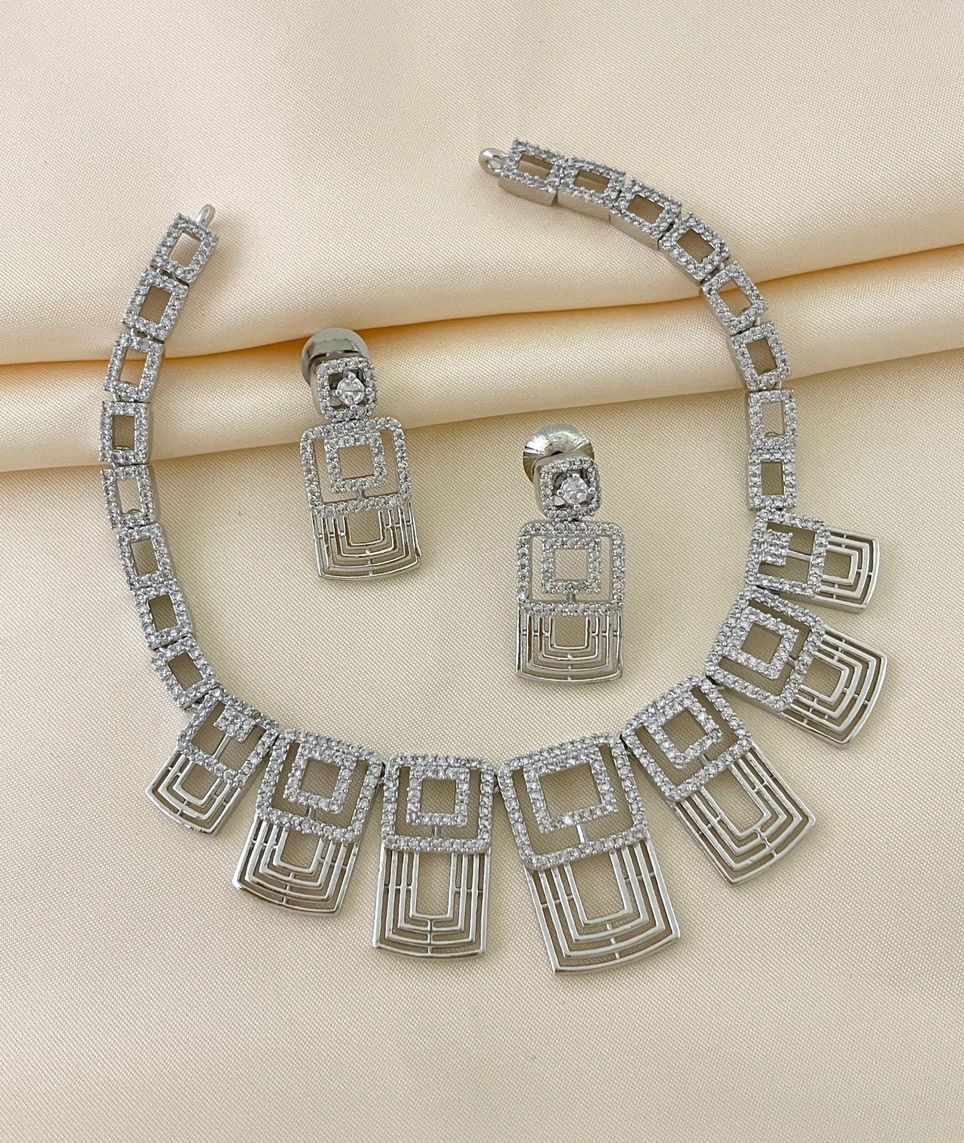 A silver necklace with geometric designs and matching earrings adorned with American diamonds.