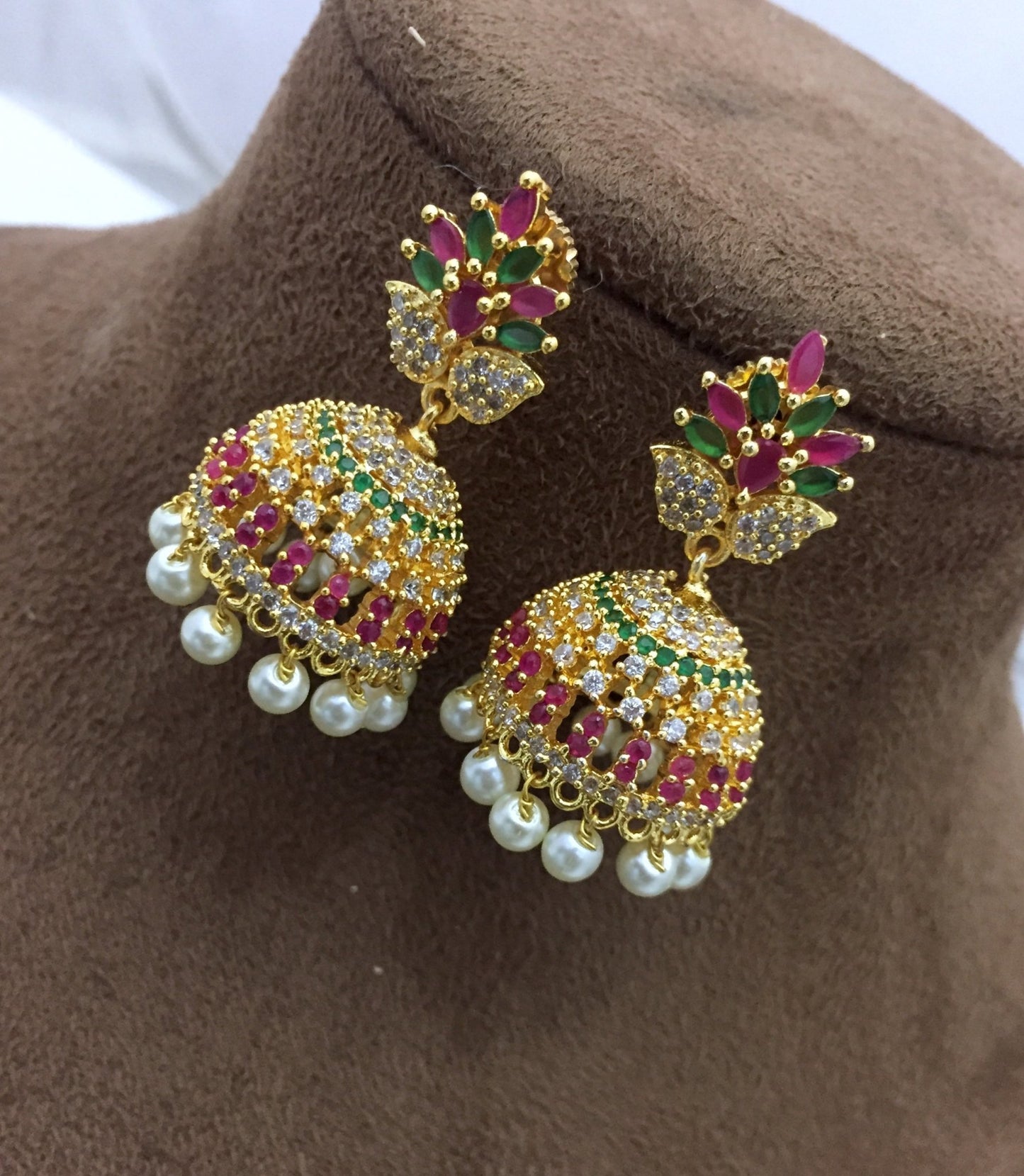 Gold jhumka earrings with CZ stones, featuring a leaf design and adorned with pearls.