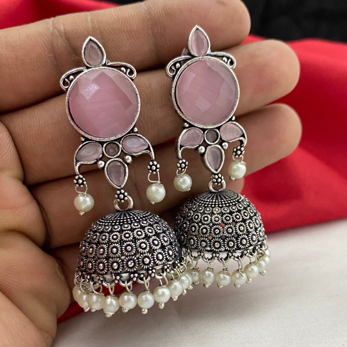 A pair of intricately designed silver jhumka earrings with pink gemstones and pearl accents.