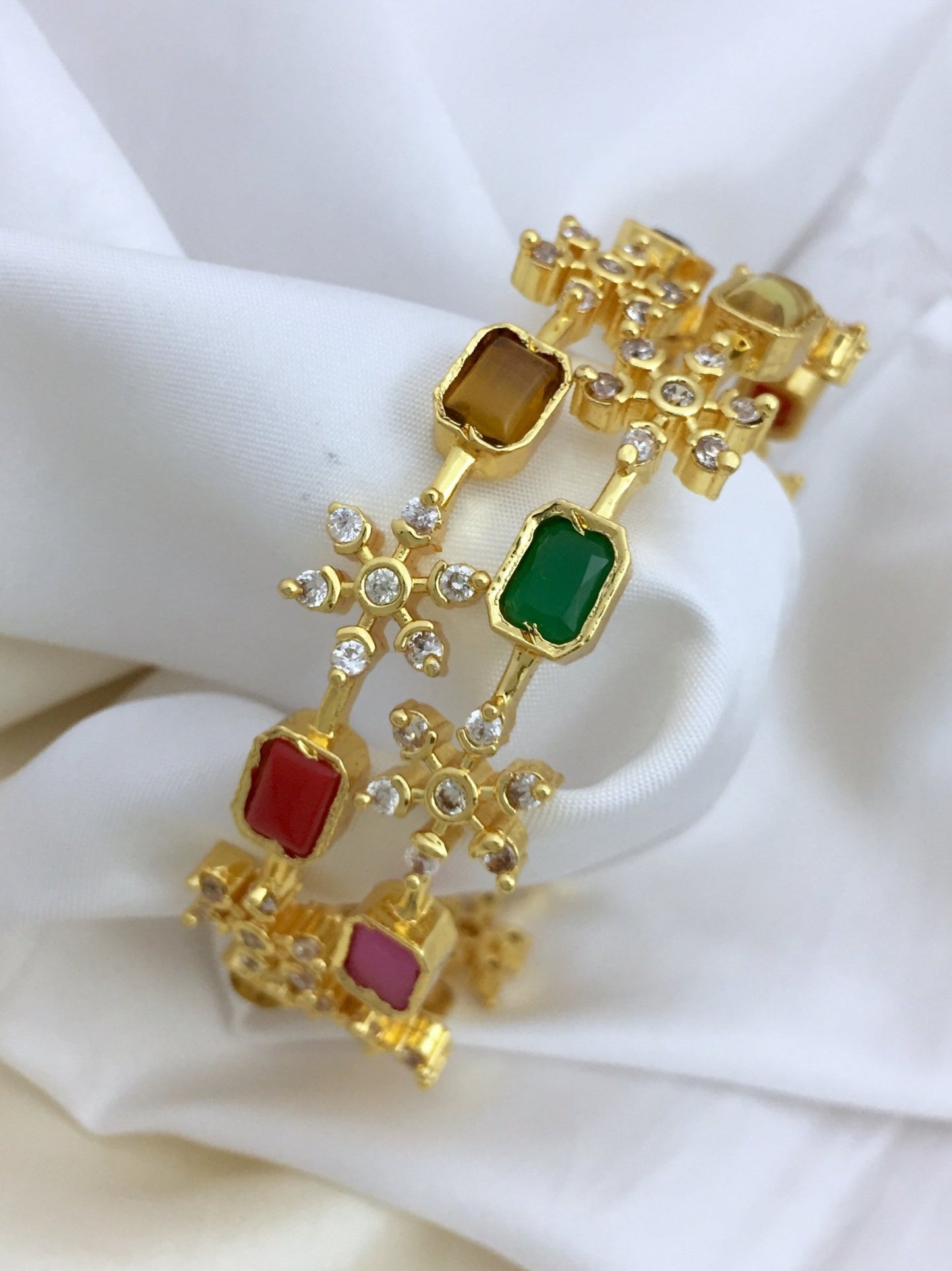 Gold bangles adorned with colorful Navratna stones and small white crystals.