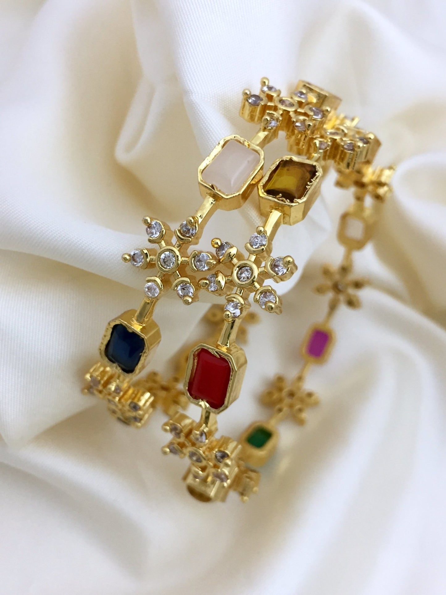 Gold bangles adorned with Navratna stones and floral designs.