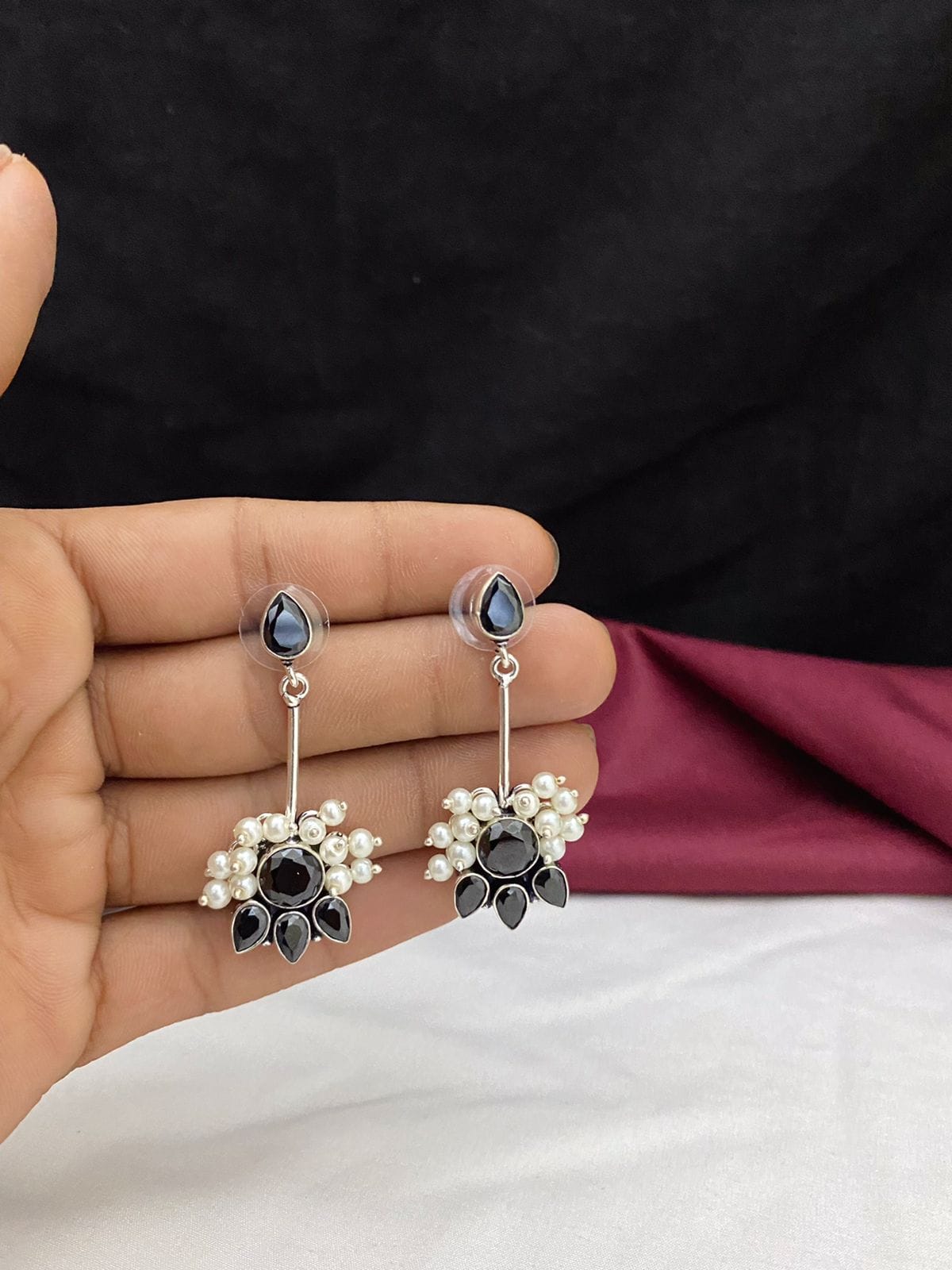 Silver drop earrings with black stones and pearl accents held in a hand.