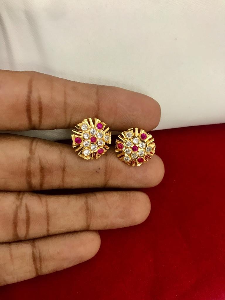 A pair of gold-tone stud earrings with red and clear stones held between fingers.