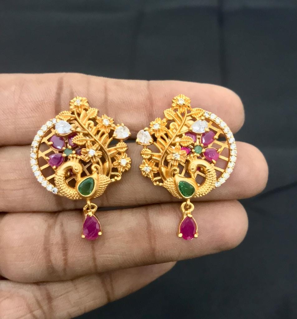 Gold stud earrings with intricate peacock design, adorned with rubies, emeralds, and diamonds, featuring a hanging ruby teardrop.