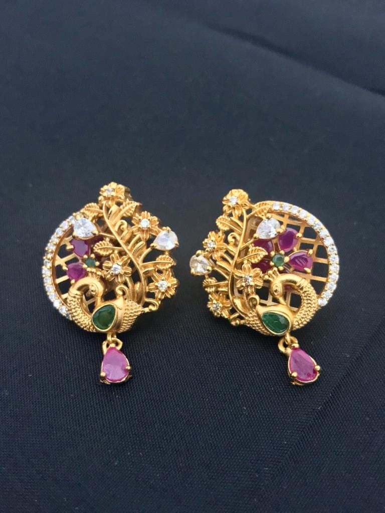 Gold stud earrings with intricate designs, featuring ruby and emerald gemstones, and floral accents.