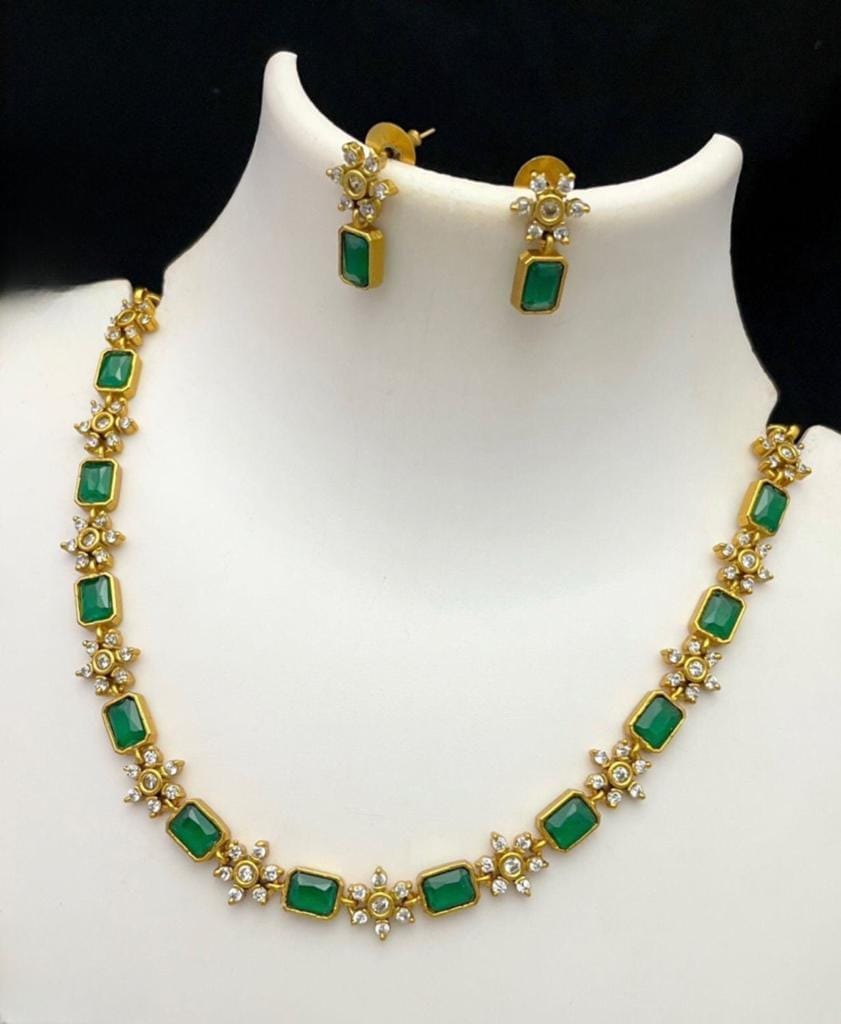 A gold necklace and earring set featuring rectangular green gemstones and small white stones.