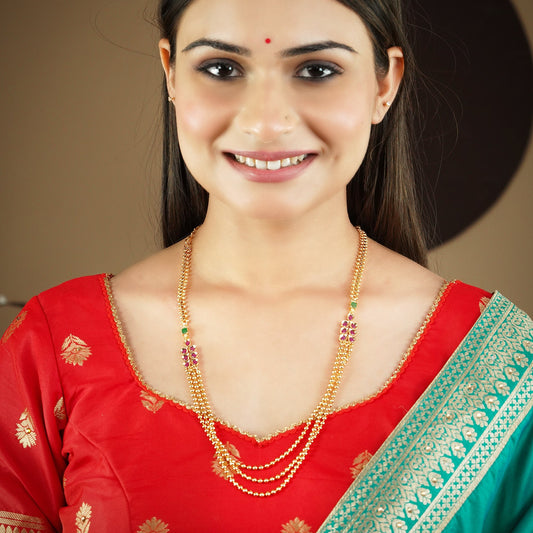 A woman wearing a red and green traditional outfit with a gold layered necklace adorned with colorful gemstones.