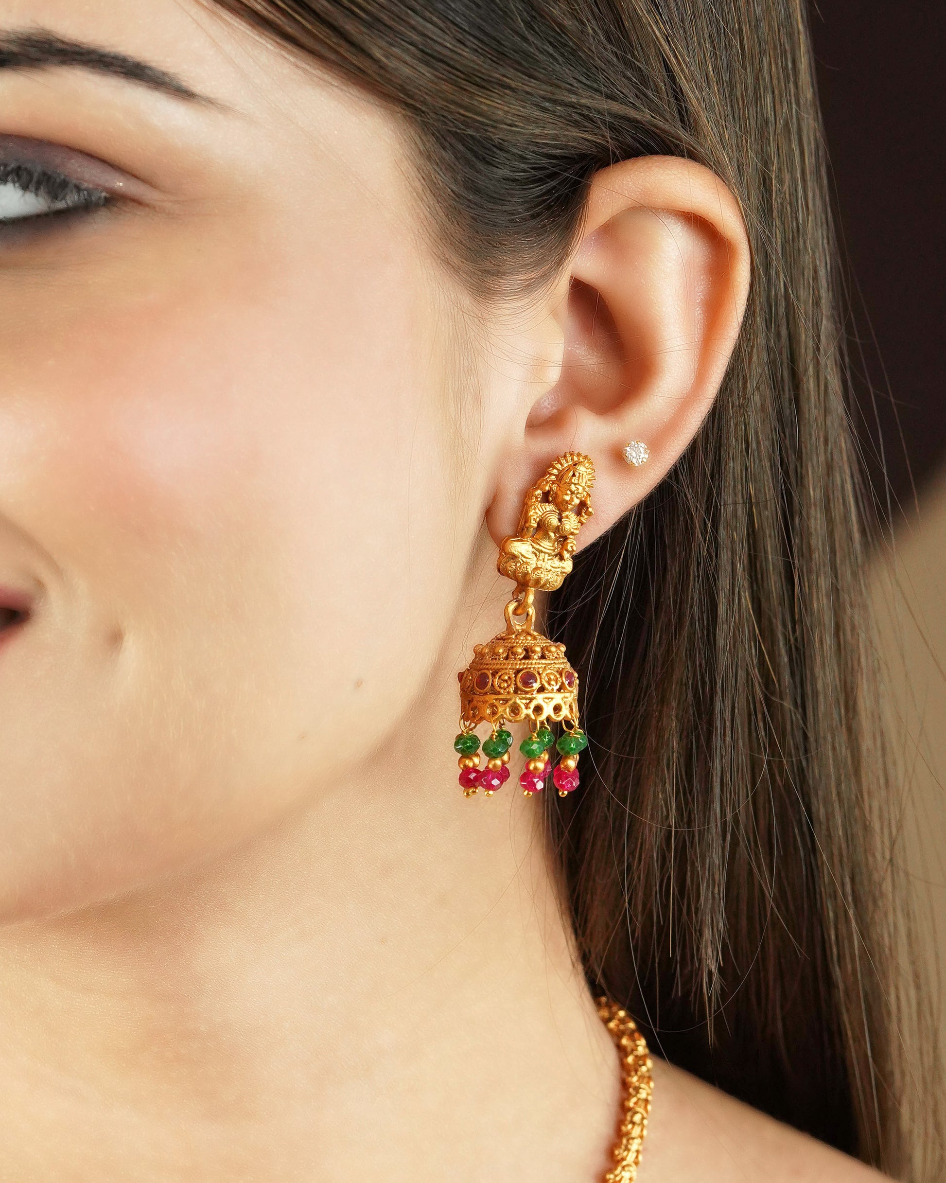 A close-up of a woman's ear wearing a gold earring with intricate designs and colorful beads hanging at the bottom.