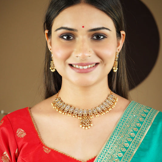 A woman wearing a traditional gold necklace with matching earrings, dressed in a red and green saree.