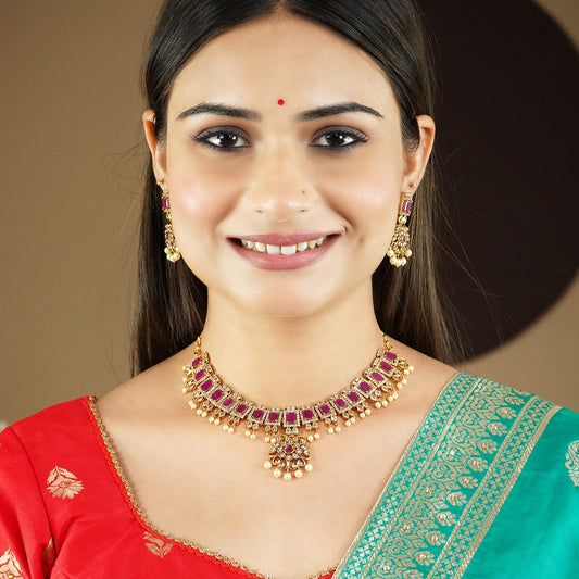 A woman wearing a traditional gold necklace with red gemstones and matching earrings. She is dressed in a red and green saree.