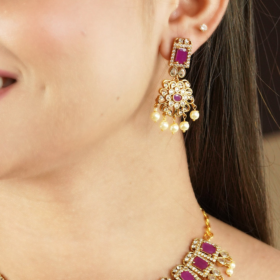 A woman wearing a gold earring with red gemstones and pearl accents.