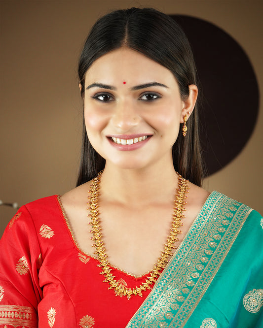 A woman wearing a red and green traditional outfit with a gold necklace and matching earrings.