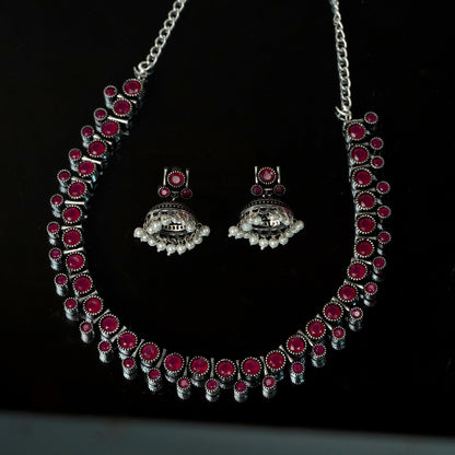 A silver necklace and matching earrings set with red gemstones and intricate detailing.