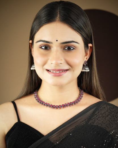 A woman wearing a black saree, silver jhumka earrings, and a pink and silver choker necklace.