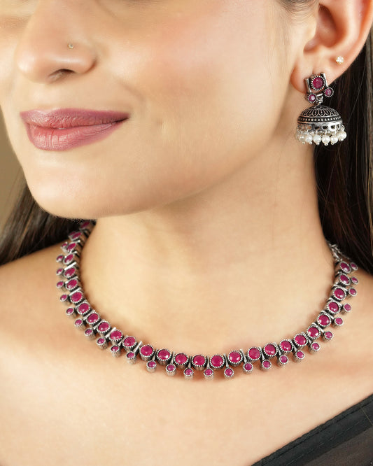 A woman wearing a silver necklace with red gemstones and matching earrings.