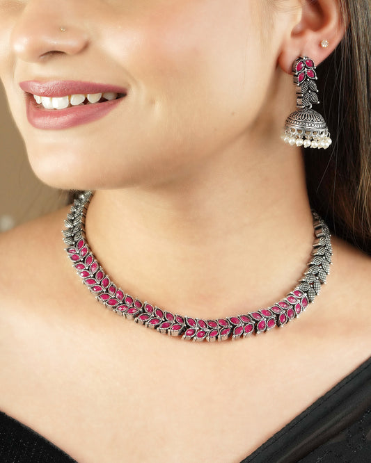 A woman wearing a silver necklace with pink gemstones and matching silver earrings.