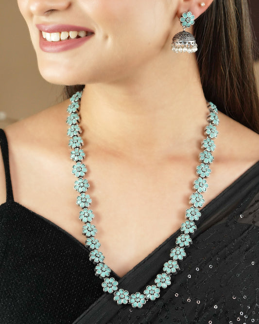 A woman wearing a black saree, a turquoise floral necklace, and matching turquoise floral earrings.