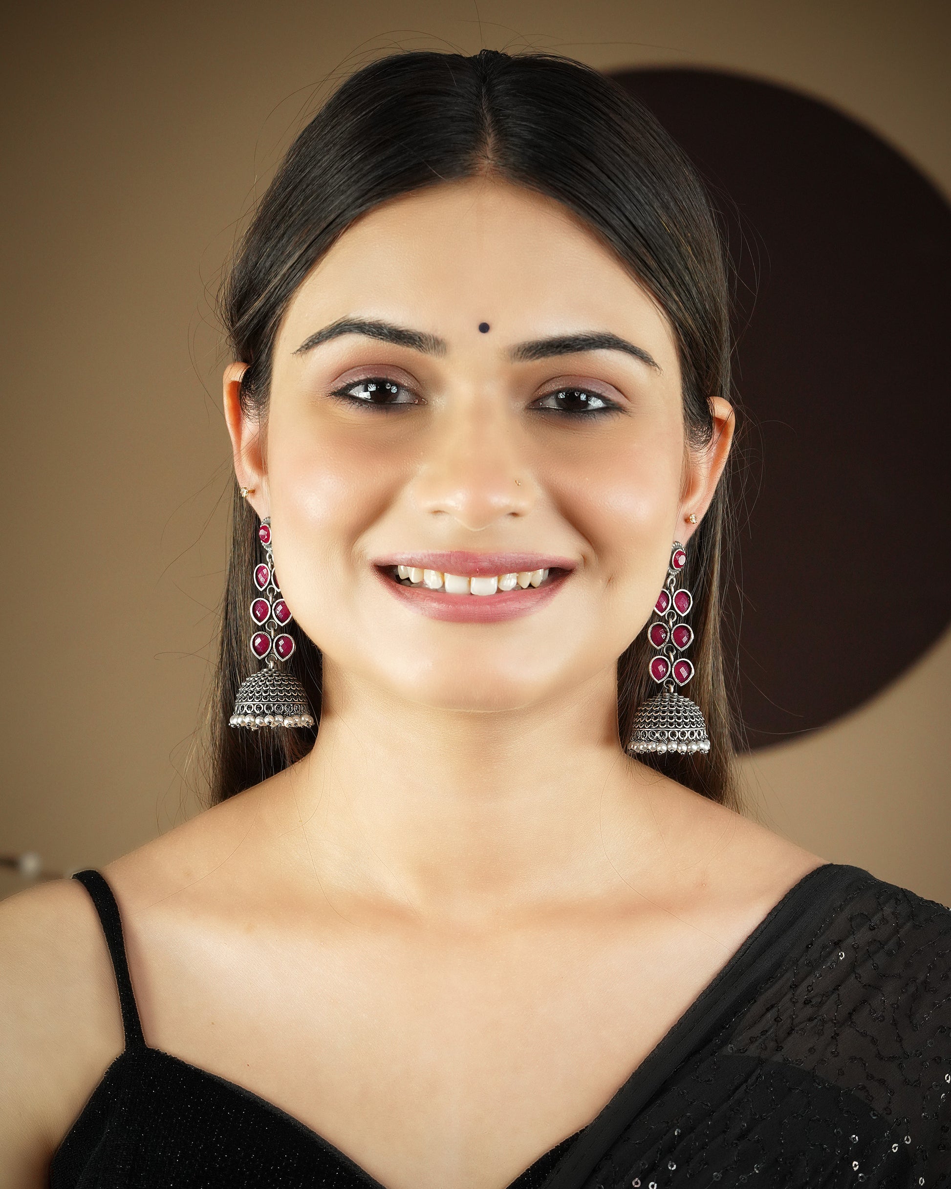A woman wearing traditional silver jhumka earrings with pink gemstones and a black saree.