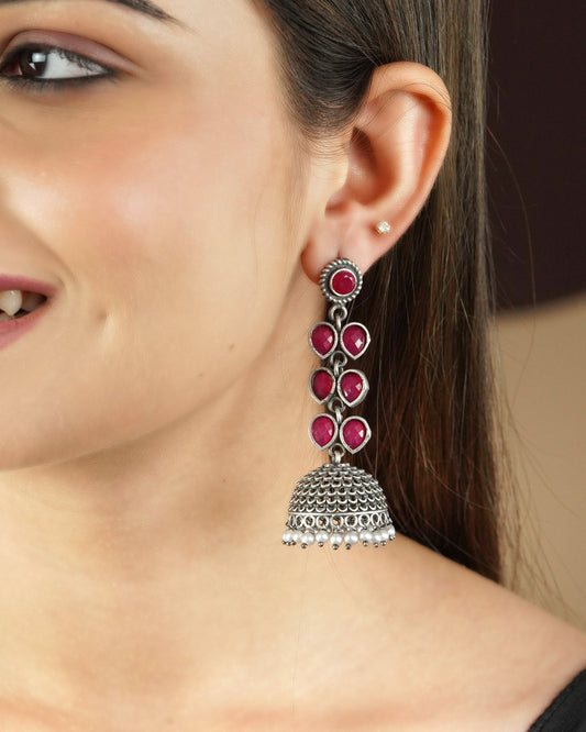 A woman wearing a silver jhumka earring with red stones.
