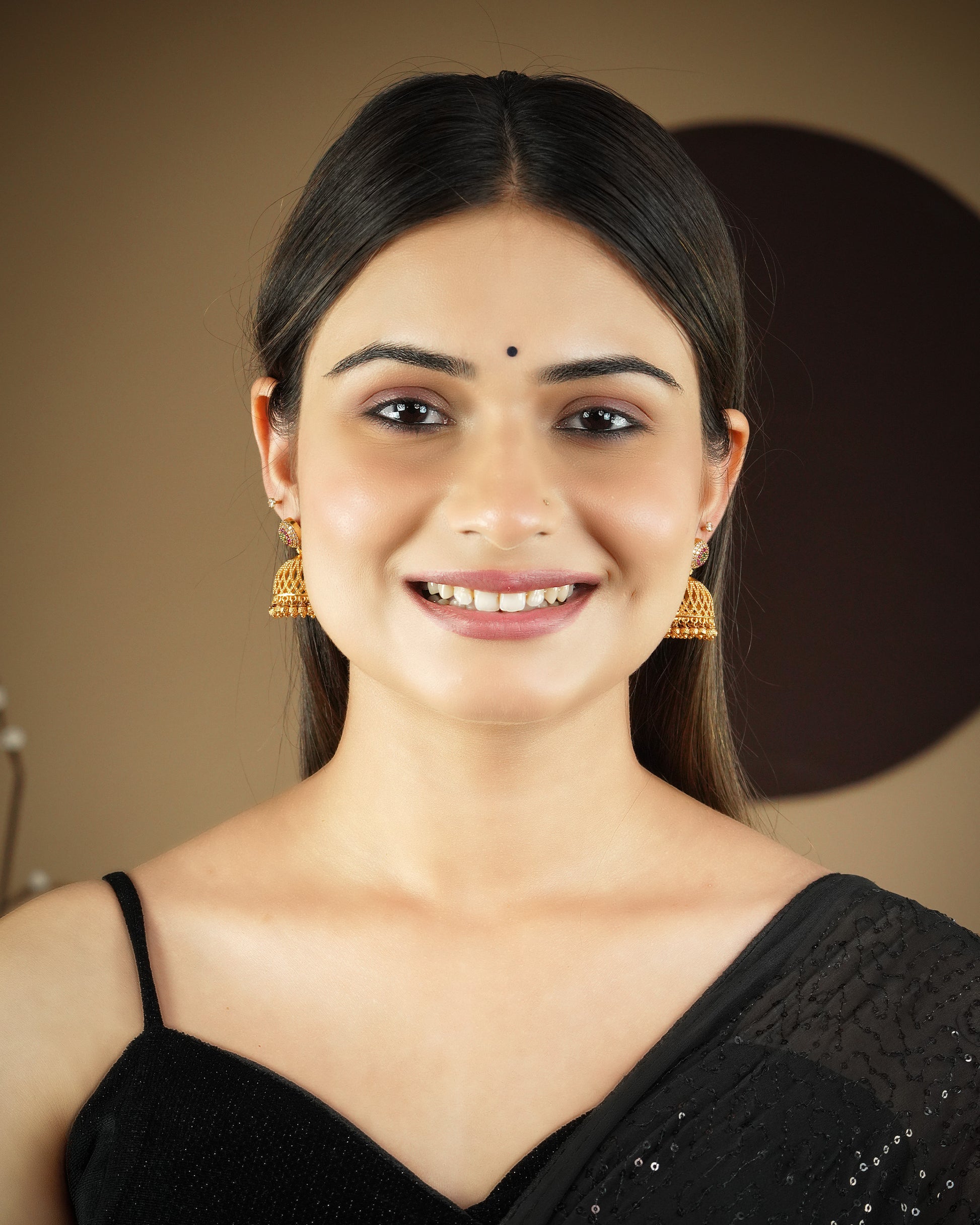 A woman wearing a black saree and gold jhumka earrings, smiling.