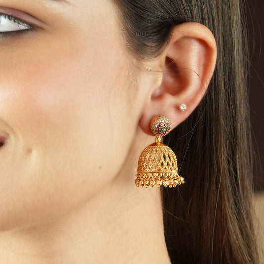 Close-up of a woman's ear wearing a gold jhumka earring with intricate detailing and a small stud earring above it.