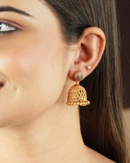 Close-up of a woman's ear wearing a gold jhumka earring with intricate detailing and small hanging beads.