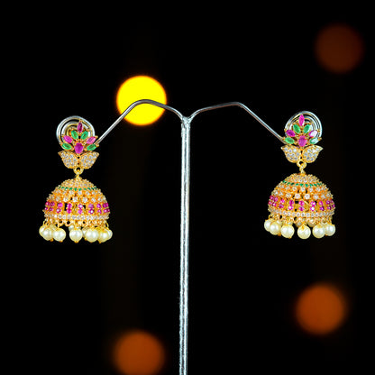 A pair of gold jhumka earrings adorned with pink and green gemstones and pearl drops.