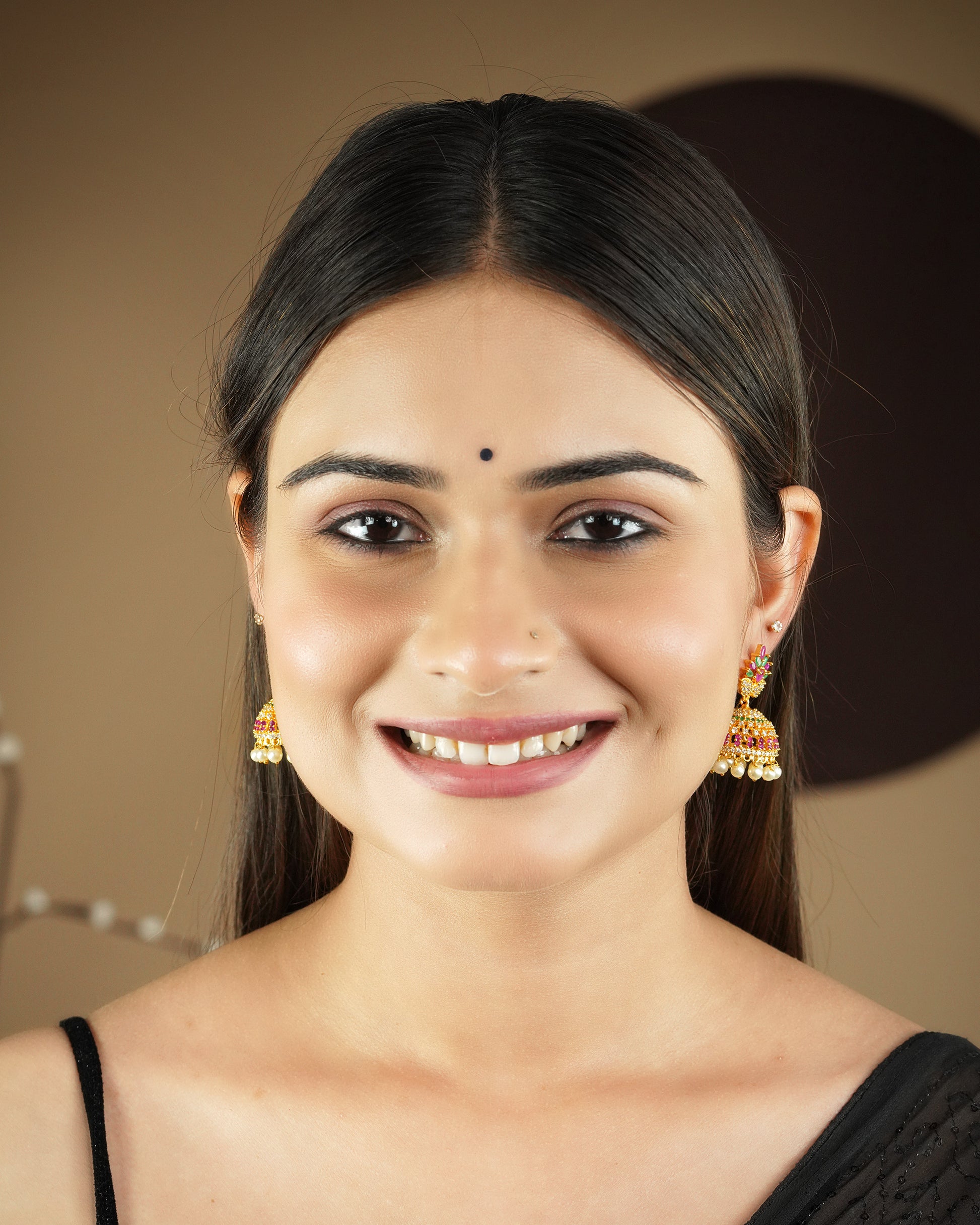 A woman wearing traditional jhumka earrings and a black bindi, smiling.