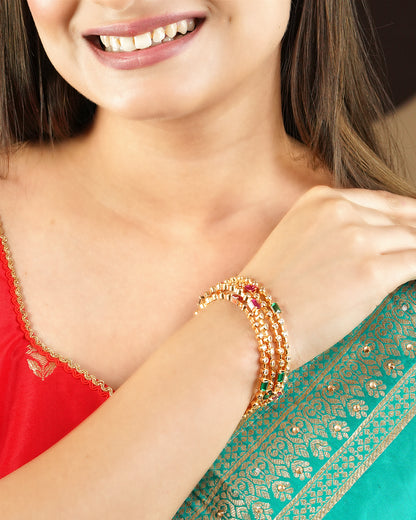 A woman wearing a red and green traditional outfit, showcasing a set of gold and multicolored beaded bangles on her wrist.