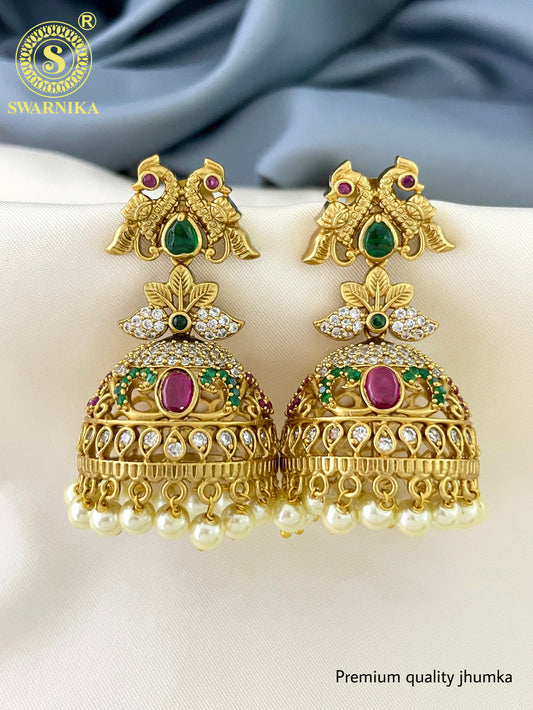 Gold jhumka earrings with intricate designs, featuring green and pink gemstones, and pearl drops.