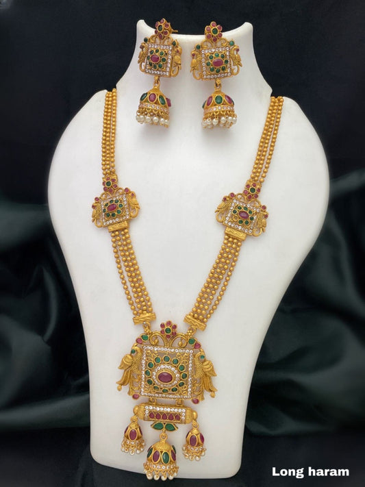 A gold long haram necklace set with intricate designs, featuring red and green gemstones, and matching earrings.