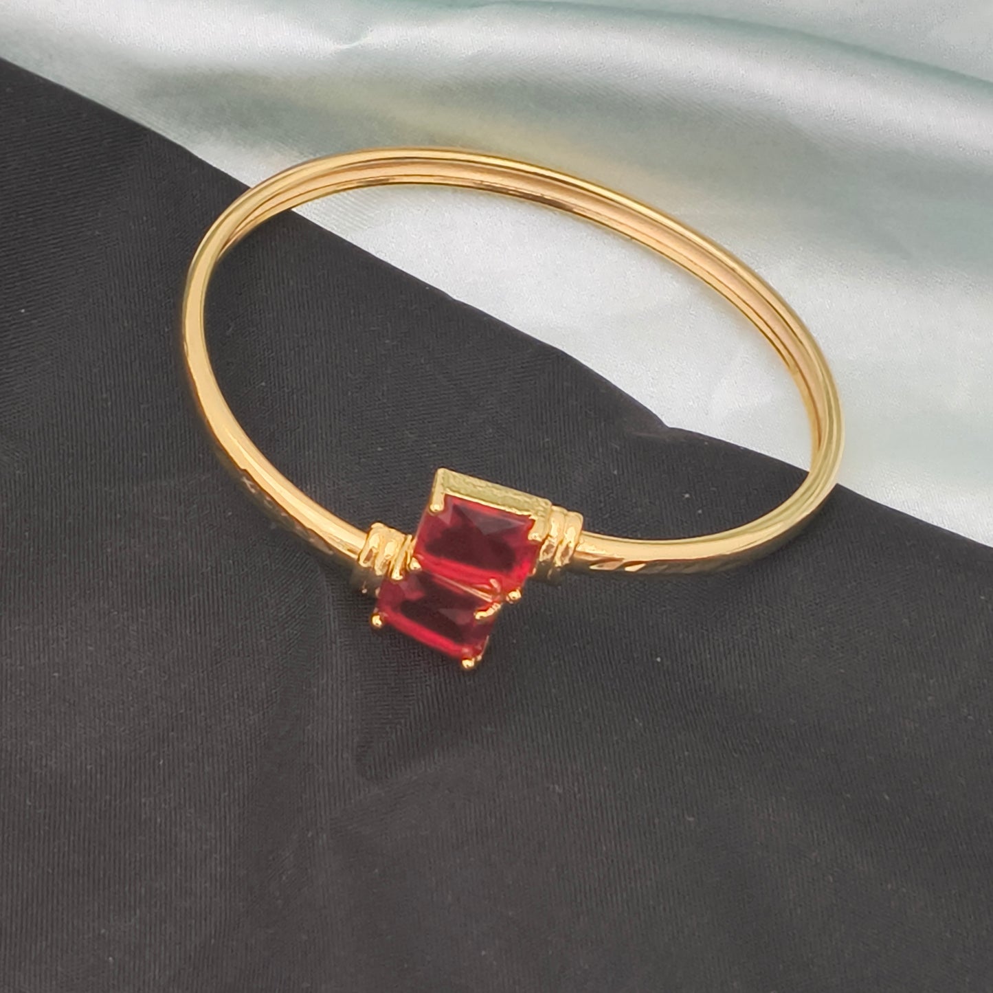 A gold bracelet featuring two rectangular red gemstones.