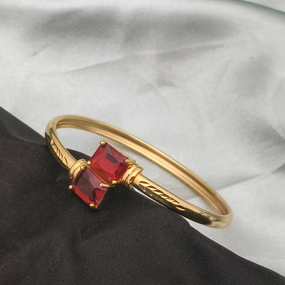 A gold bracelet featuring two square red gemstones.