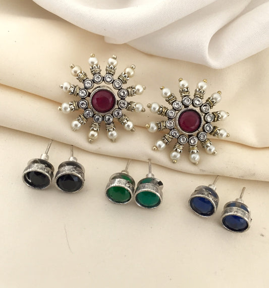 A set of earrings, including a pair of large, ornate earrings with a central red stone surrounded by smaller white and silver stones, and three pairs of smaller stud earrings with black, green, and blue stones.